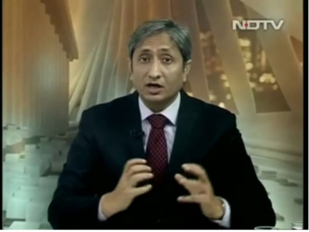 A male news anchor of Indian descent speaking directly into the camera